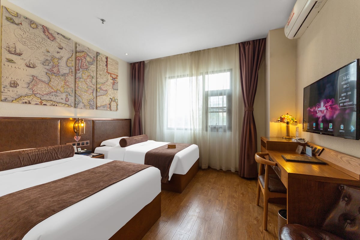 A hotel room with two beds, a desk, a chair, a TV, and a large map on the wall.