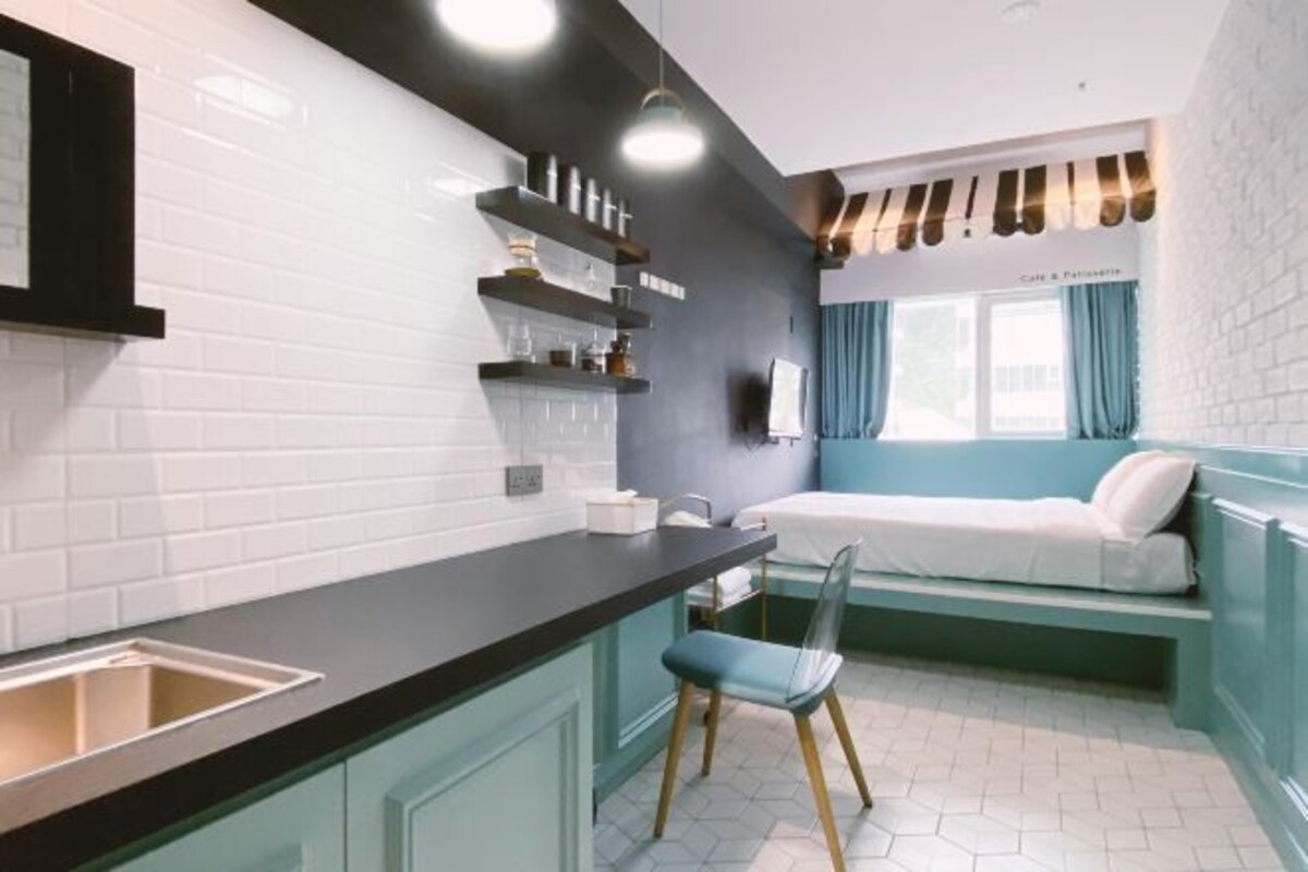 A compact kitchen with a black countertop, white tiled backsplash, and a built-in bench with a white mattress.