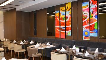 Un restaurante con varias mesas y sillas, una zona de estar con un largo banco, y coloridas obras de arte abstracto en la pared.