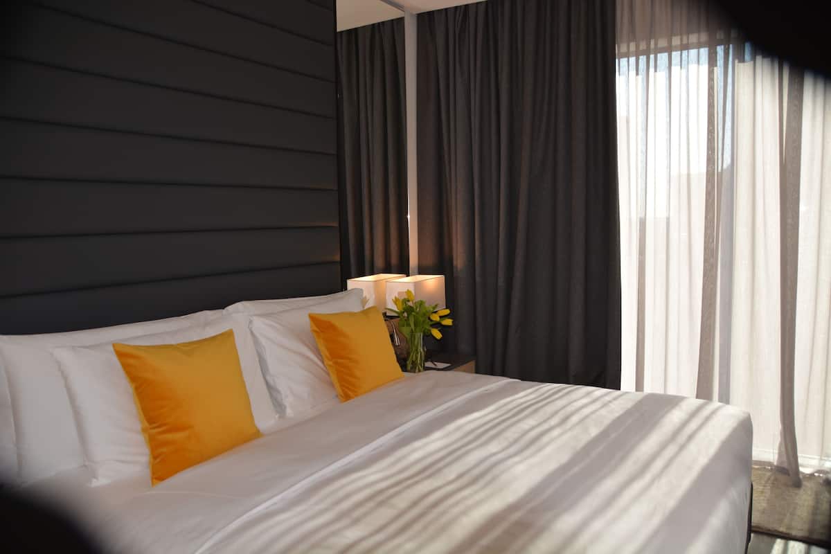 Una habitación de hotel con una cama grande, dos almohadas, una mesita de noche con lámpara y un florero con flores.