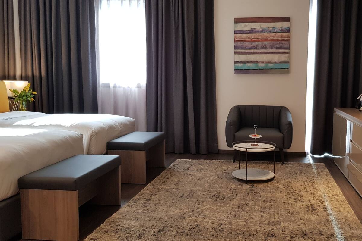 Habitación de hotel con cama, escritorio, silla, televisor y una pequeña mesa con un florero.