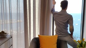 Una sala de estar moderna con un ventanal grande, un sofá con un cojín amarillo, una mesa de centro y un par de zapatos sobre la alfombra.