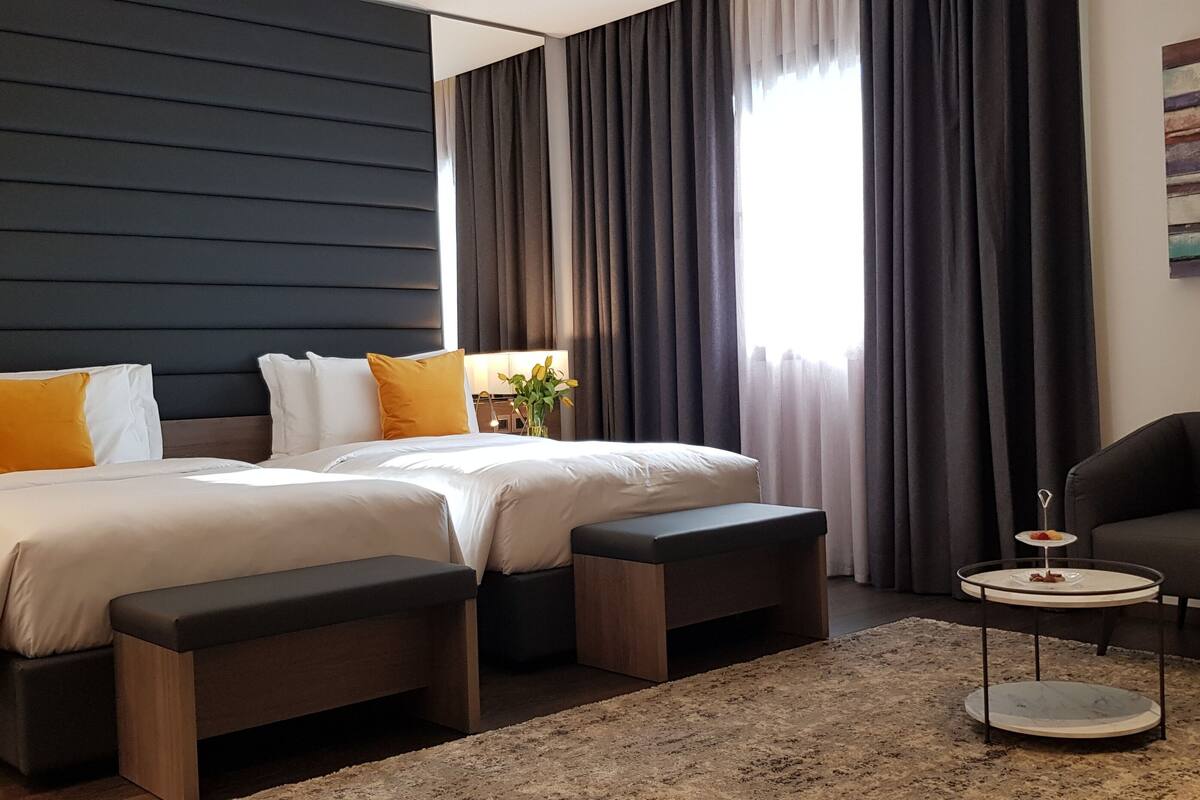 Una habitación de hotel moderna con una cama grande, dos mesitas de noche, una pequeña mesa redonda y un sofá.