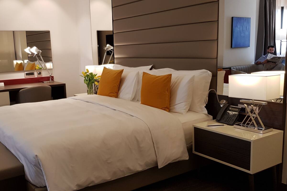 Una habitación de hotel con cama, mesita de noche, lámpara y espejo.