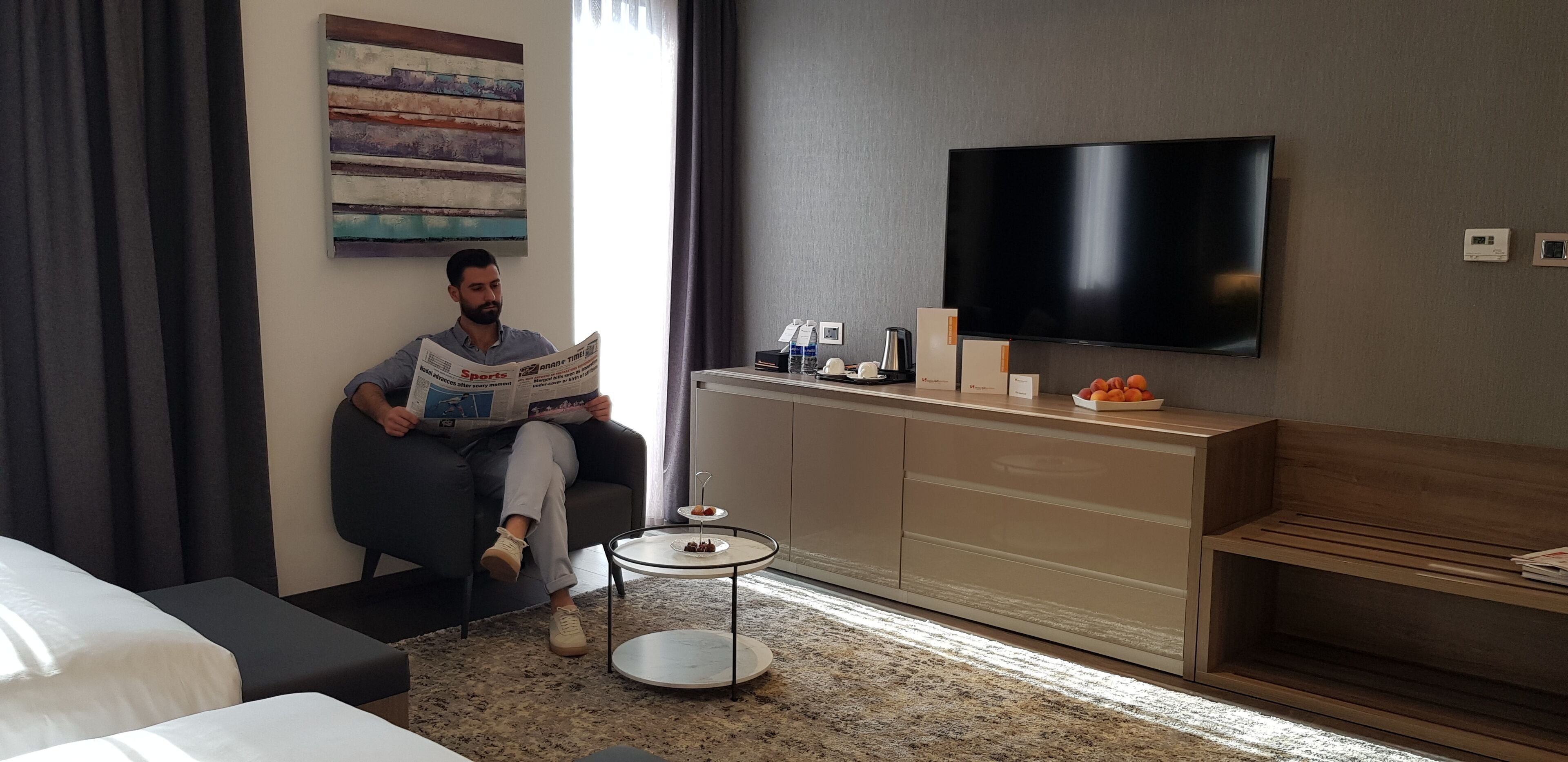 Habitación de hotel con sofá, televisión, una pequeña mesa con una bandeja de aperitivos, cafetera y armario.