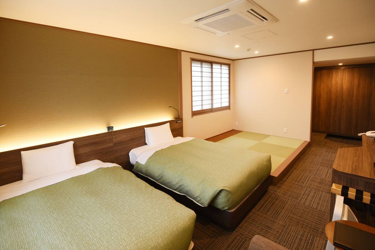 Habitación de hotel con dos camas, un escritorio y una ventana con persianas.