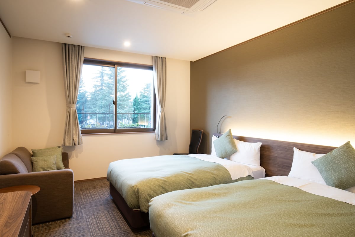Habitación de hotel con dos camas, un sofá, un escritorio y una ventana con cortinas.