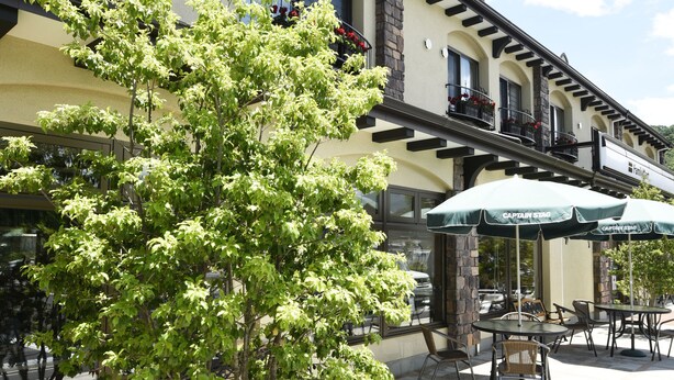 A building with outdoor seating, a tree planter, and a balcony with red flowers.