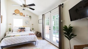 Ein Schlafzimmer mit einem Bett, einem Deckenventilator, einem Fernseher und einer Schiebetür zu einem Außenbereich.