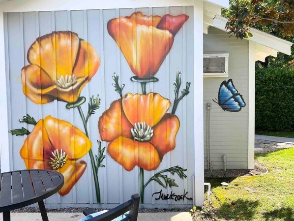 Un mural de amapolas en una pared, una escultura de mariposa y una mesa con una silla.