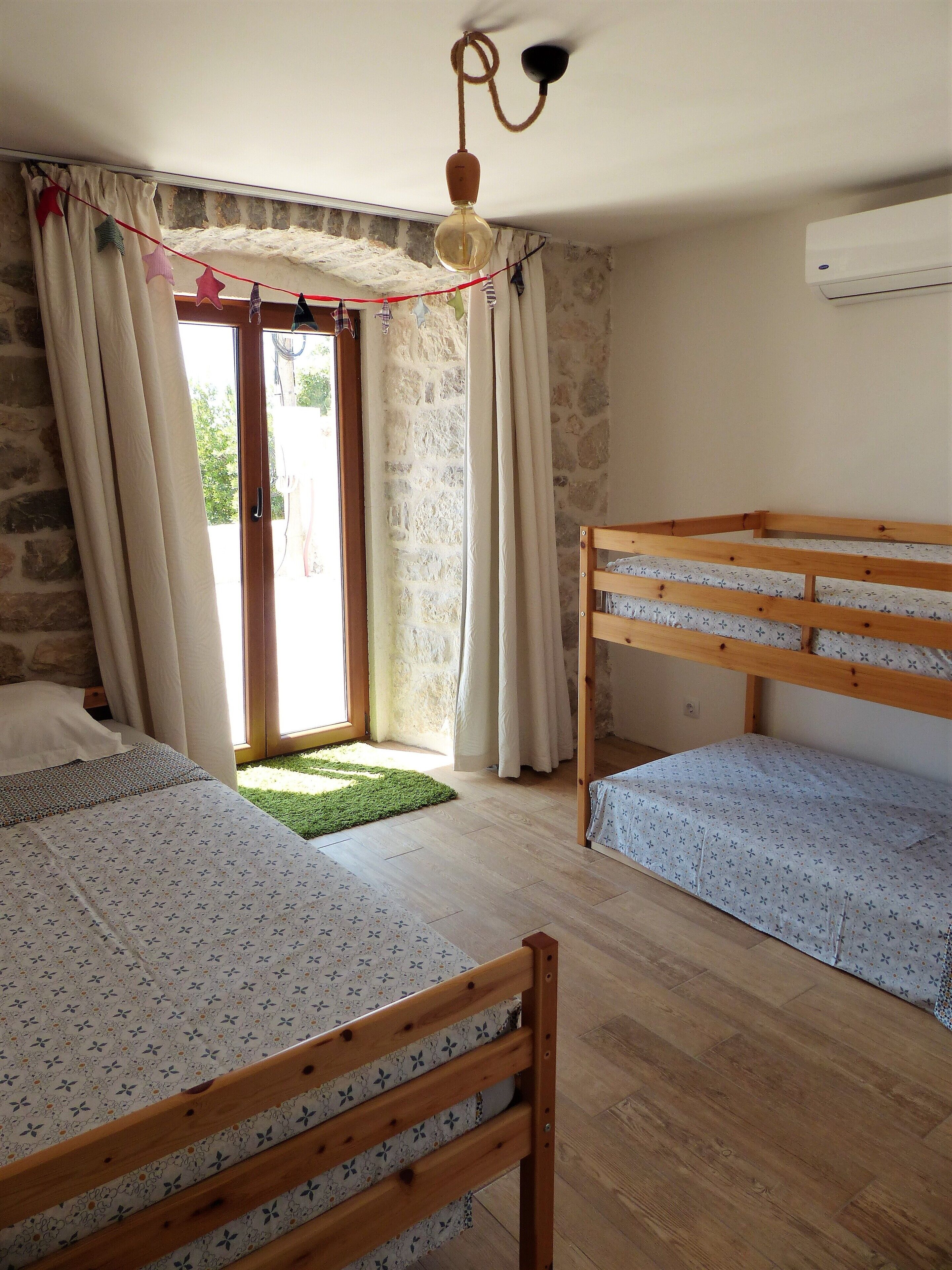 A room with two wooden bunk beds, a green rug, a stone wall, and a window with curtains.