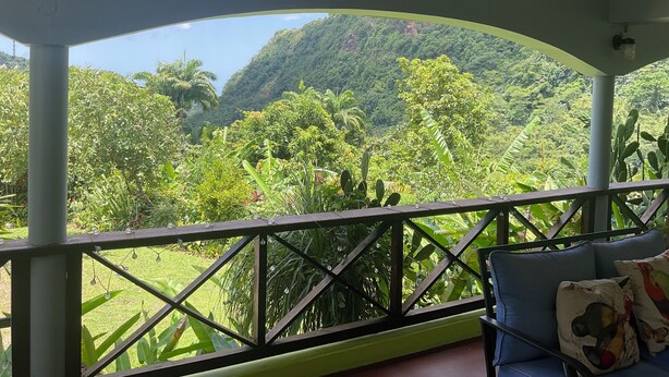 Un espace extérieur aménagé, abrité et doté de sièges, offrant une vue sur une végétation luxuriante et des collines.