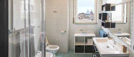 Een moderne badkamer met een douchecabine van glas, twee toiletten, een wastafel en een wastafelmeubel met spiegel.
