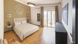 Un dormitorio con una cama, una silla, un aparador y un ventanal con cortinas.