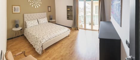 Ein Schlafzimmer mit Bett, Sessel, Schminktisch und einem großen Fenster mit Vorhängen.