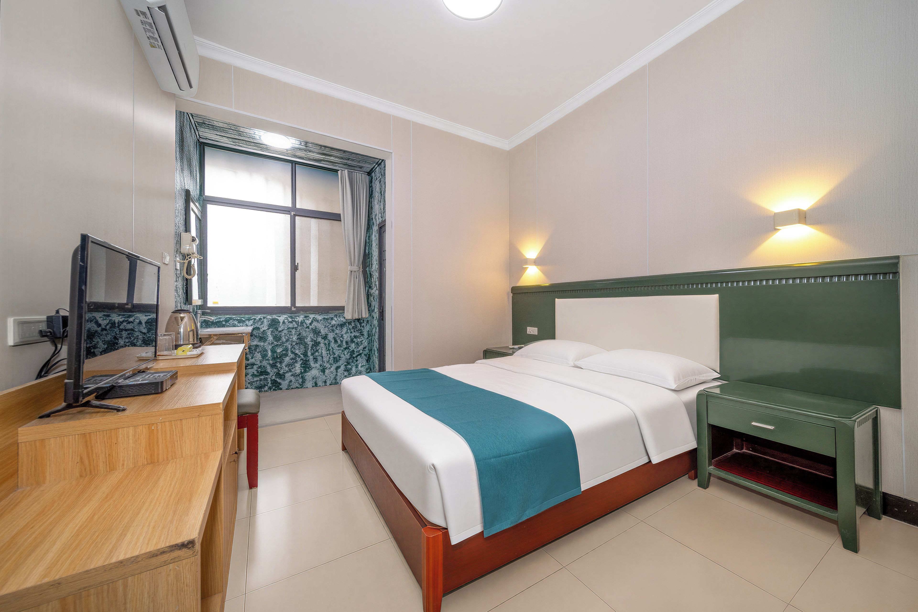 Une chambre d’hôtel avec un lit, une table de chevet, un bureau avec un ordinateur et une fenêtre avec des rideaux.