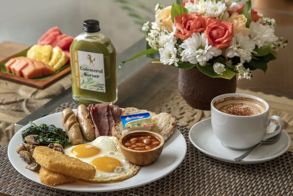 A breakfast plate with eggs, beans, sausages, and toast, a bottle of Colescerol Burner, a cup of coffee, and a floral arrangement.