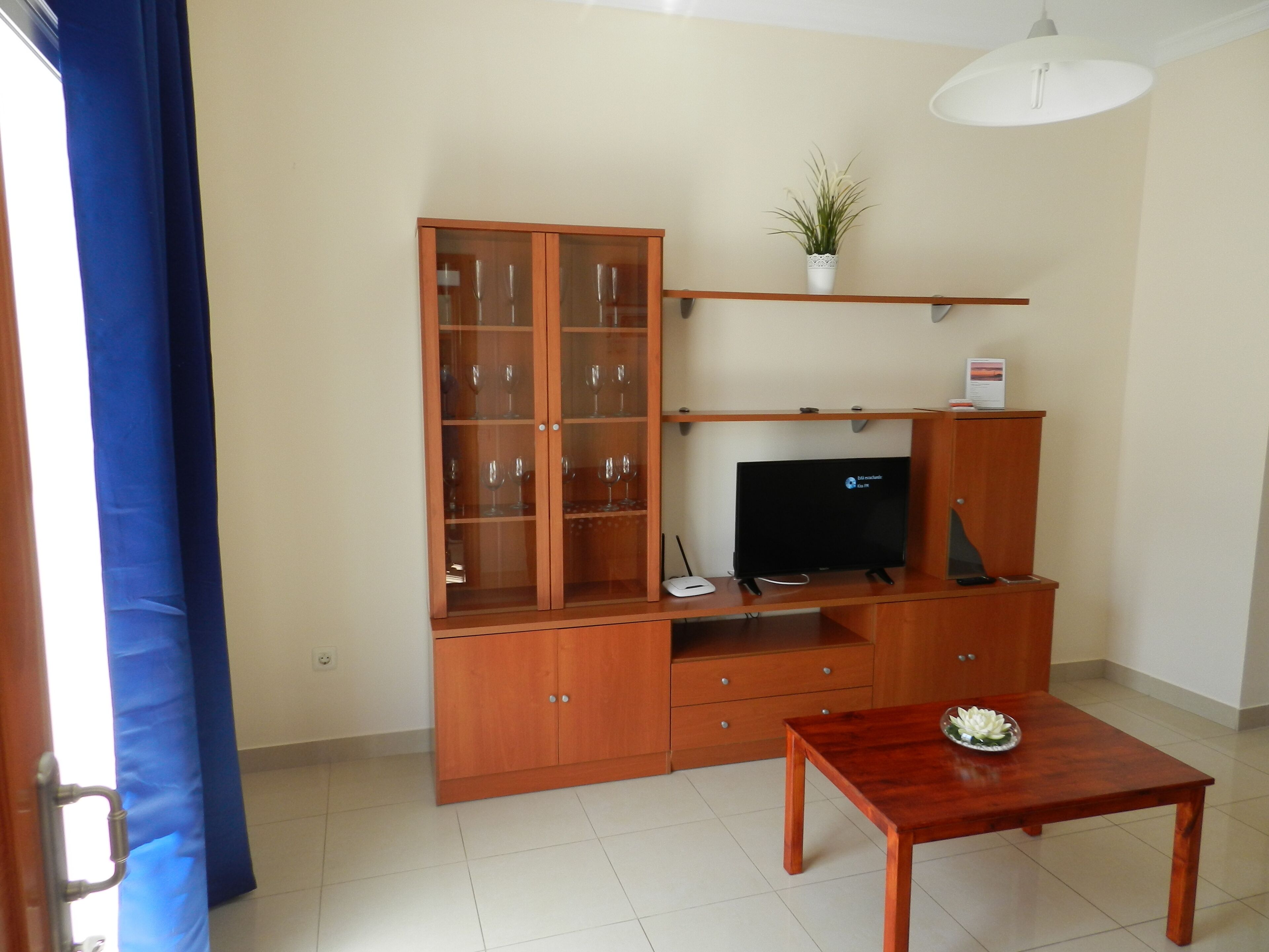 A living room with a wooden cabinet, a television, a small table, and a potted plant.