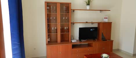 A living room with a wooden cabinet, a television, a small table, and a potted plant.