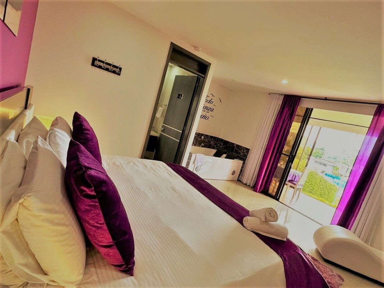 A hotel room with a bed, pillows, a chair, a window with curtains, and a door.