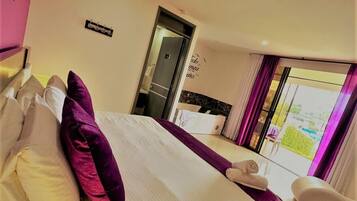 A hotel room with a bed, pillows, a chair, a window with curtains, and a door.