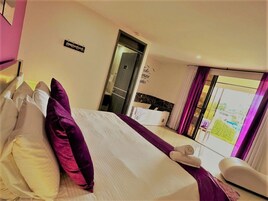 A hotel room with a bed, pillows, a chair, a window with curtains, and a door.