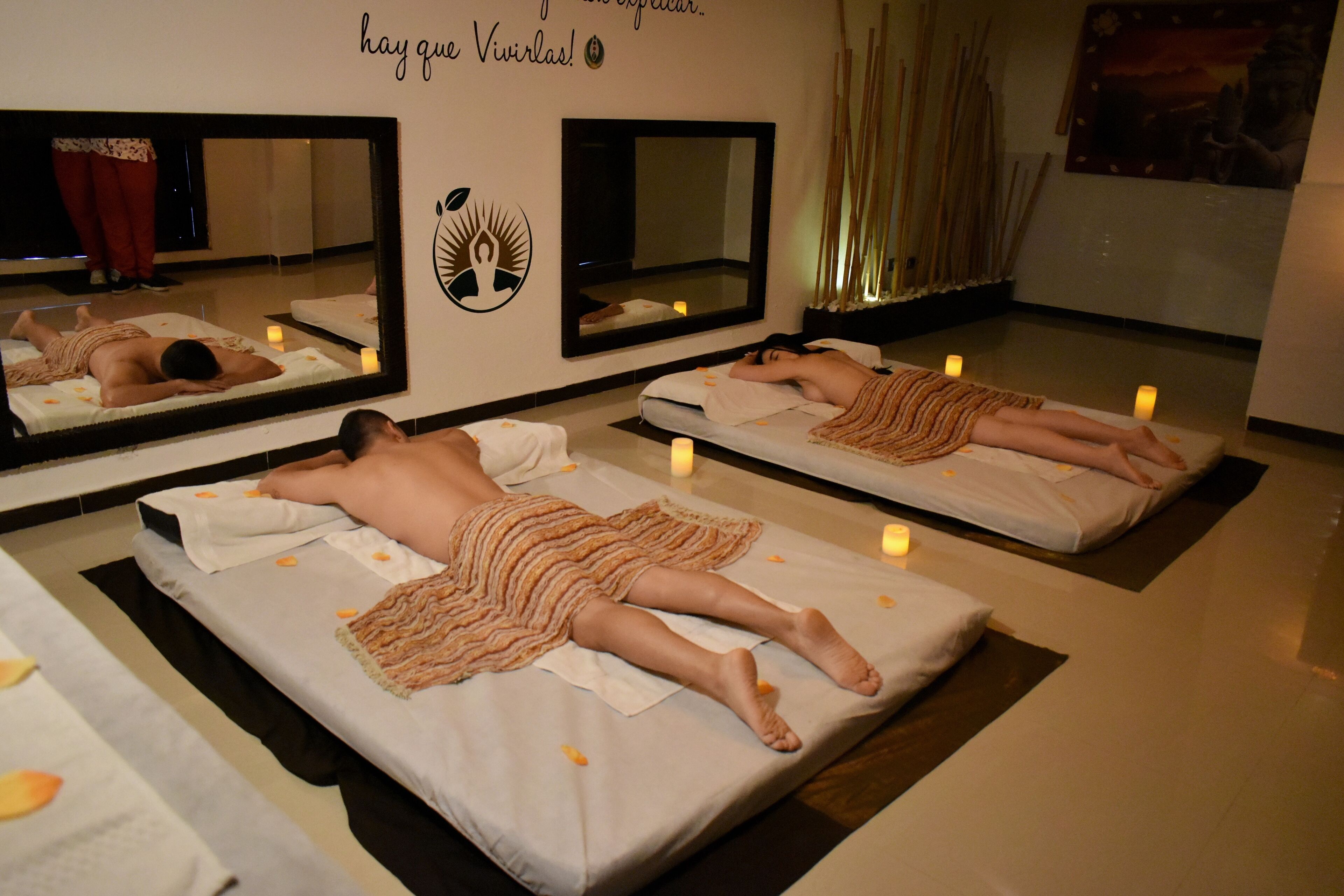 A room with massage therapy beds, candles, and a mirror reflecting the room.