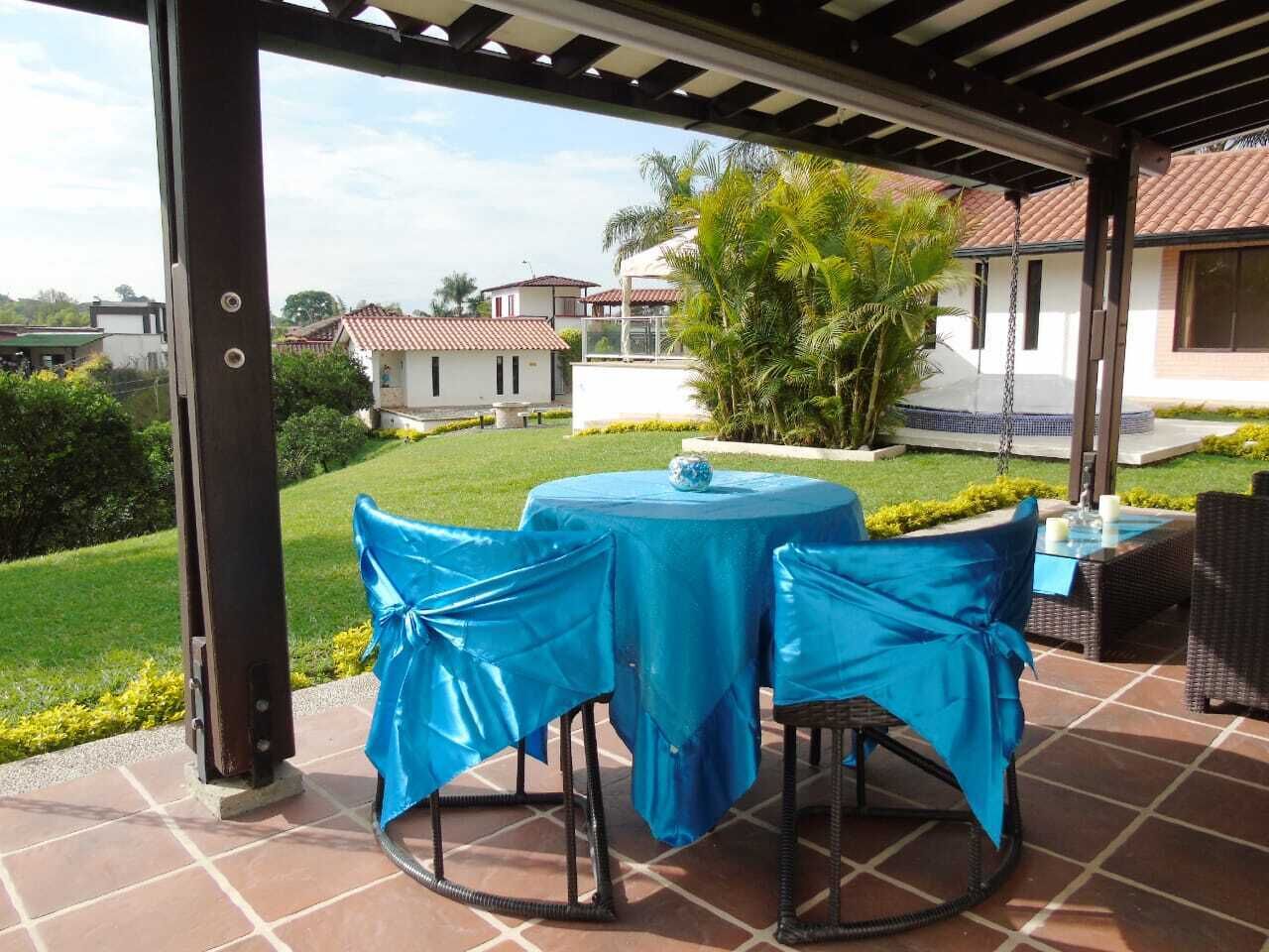 Un patio al aire libre con un área cubierta, amoblado con una mesa redonda y sillas, y vistas del barrio circundante.