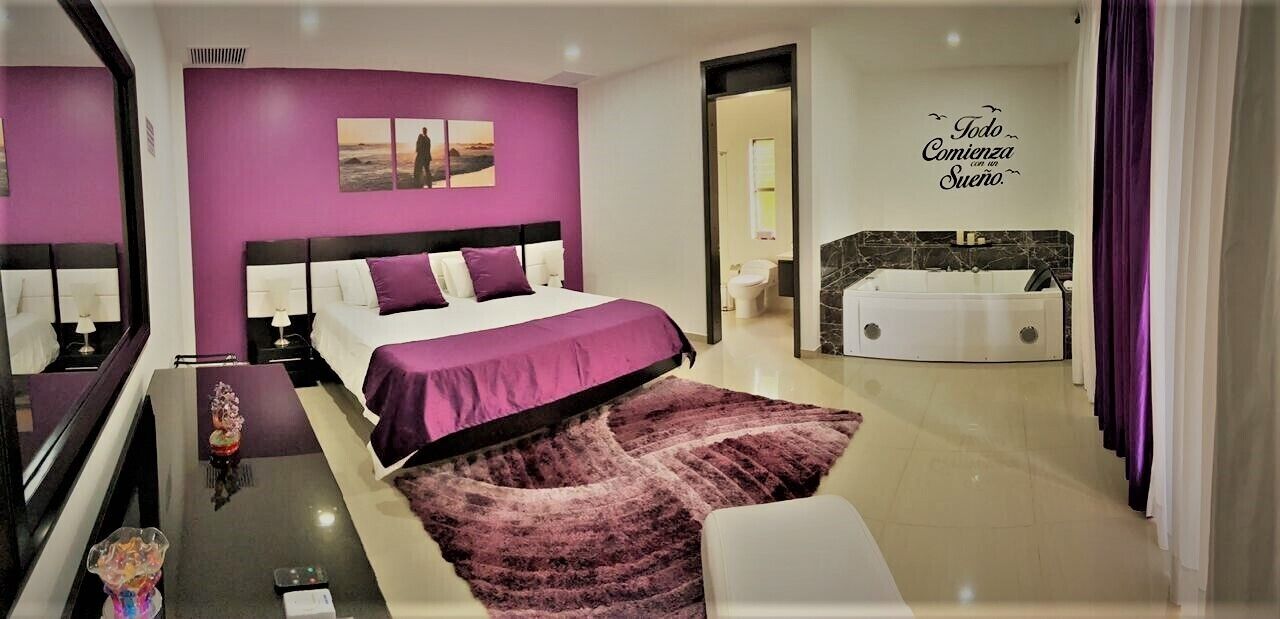 A modern bedroom with a large bed, a bathroom with a bathtub, and a motivational wall quote.