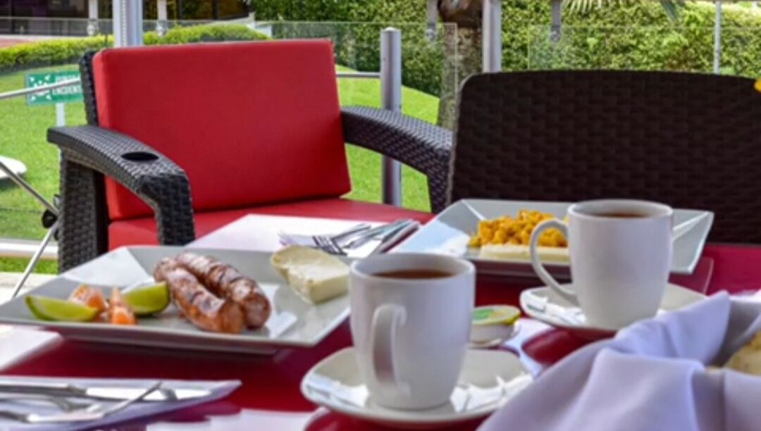 Une table à manger avec une chaise rouge, une tasse à café blanche et une assiette contenant de la nourriture et des boissons.