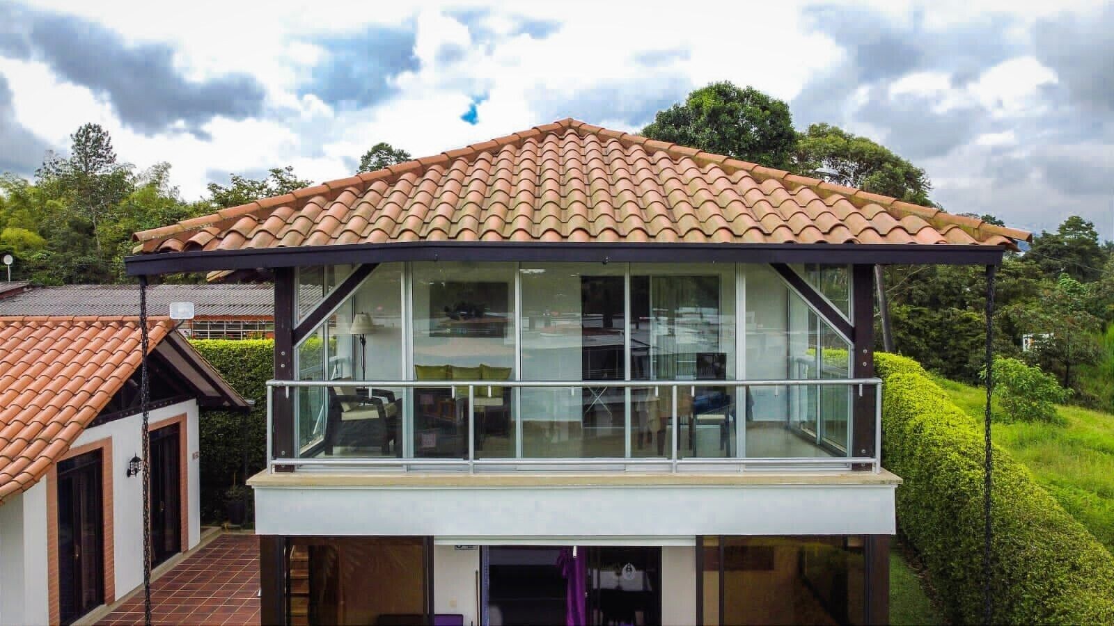 A two-story house with a balcony, large windows, and a tiled roof.