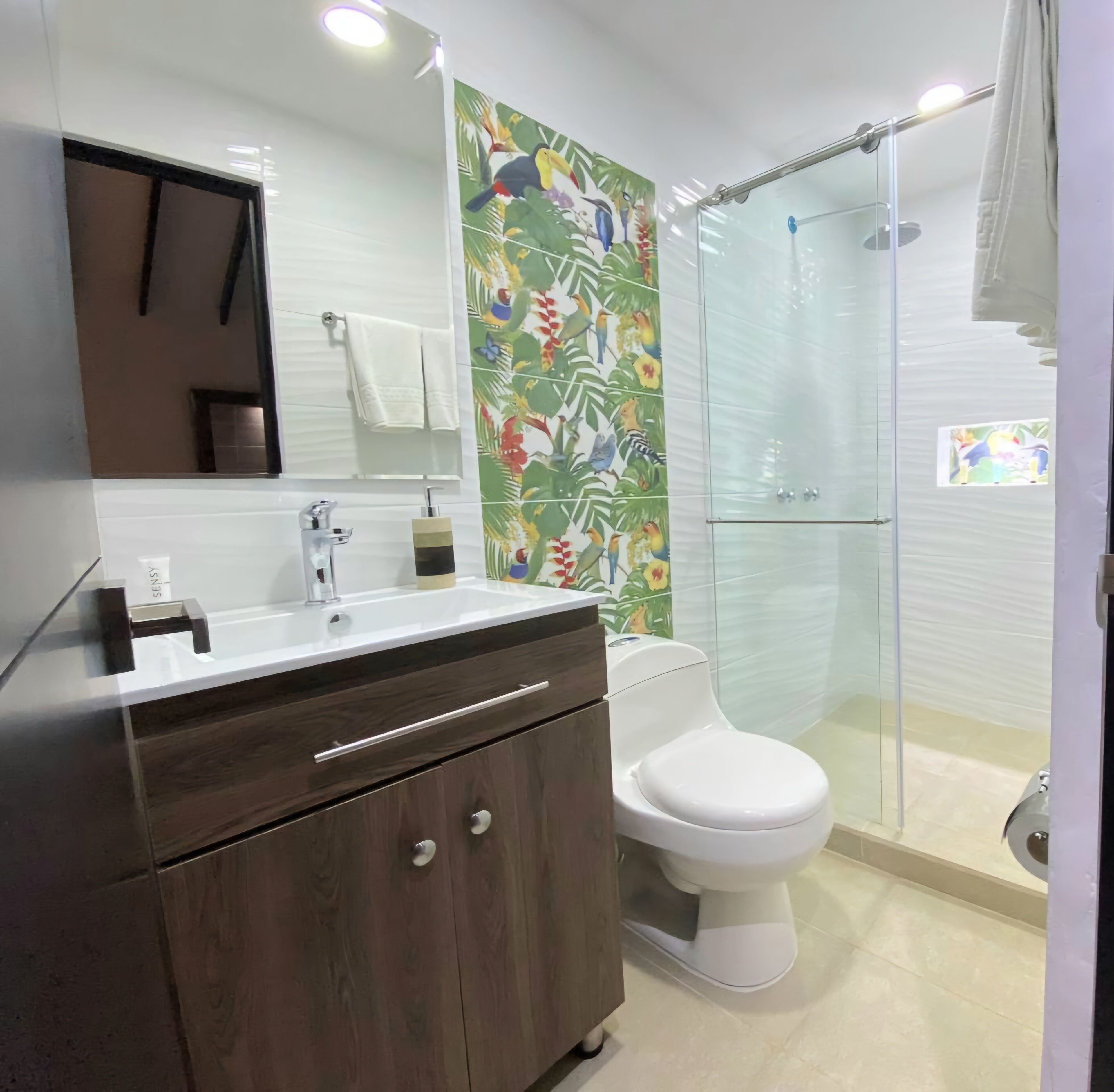 A modern bathroom with a white sink, dark wooden vanity, a toilet, and a glass shower enclosure.