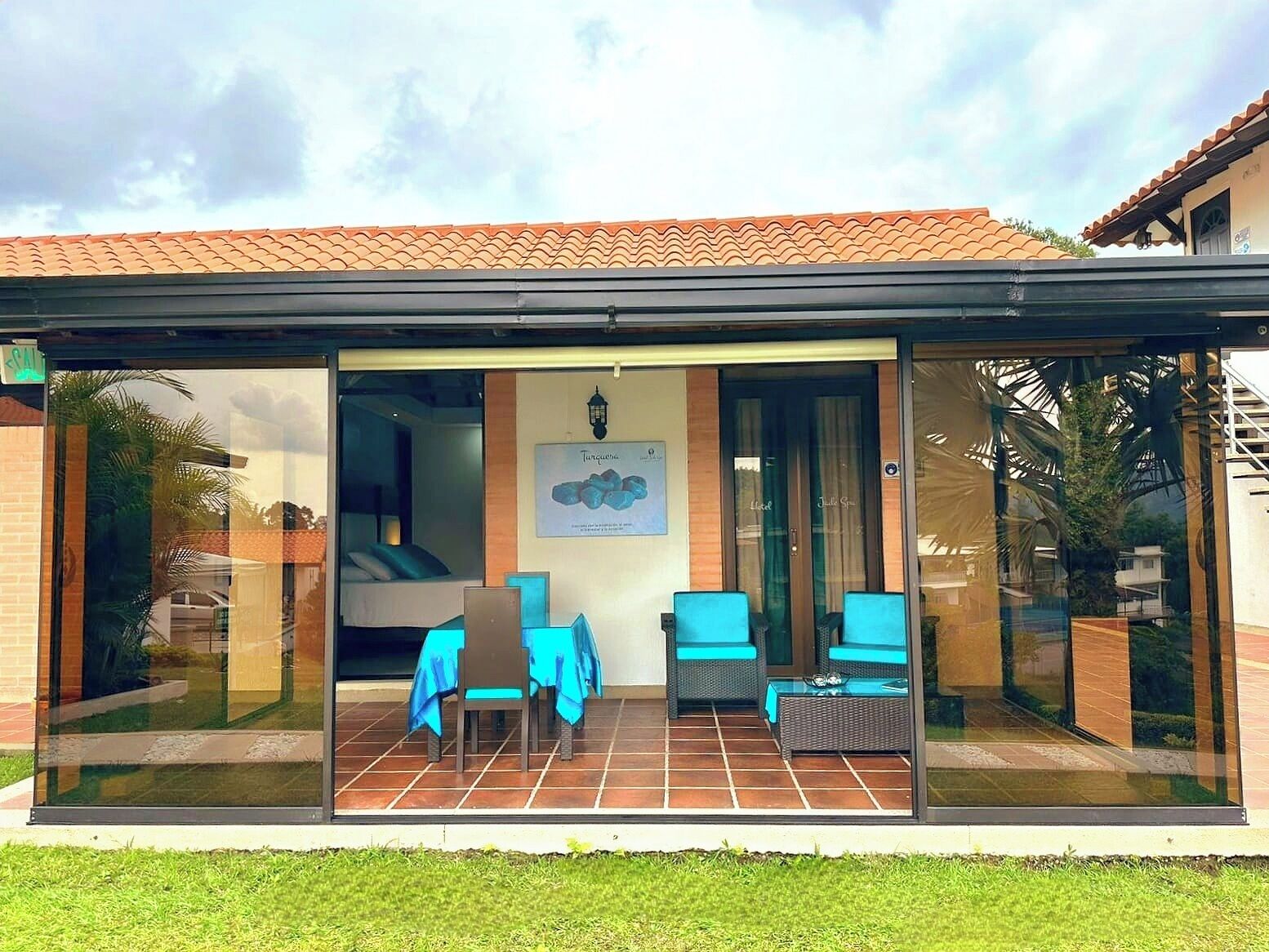 A modern building with a glass entrance, a patio with blue furniture, and a tiled roof.