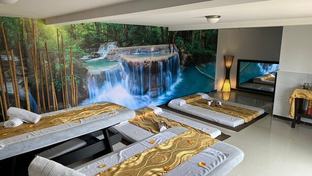 Une salle de spa équipée de tables de massage, ornée d’une grande fresque représentant une cascade, et dotée d’un téléviseur posé sur un meuble.