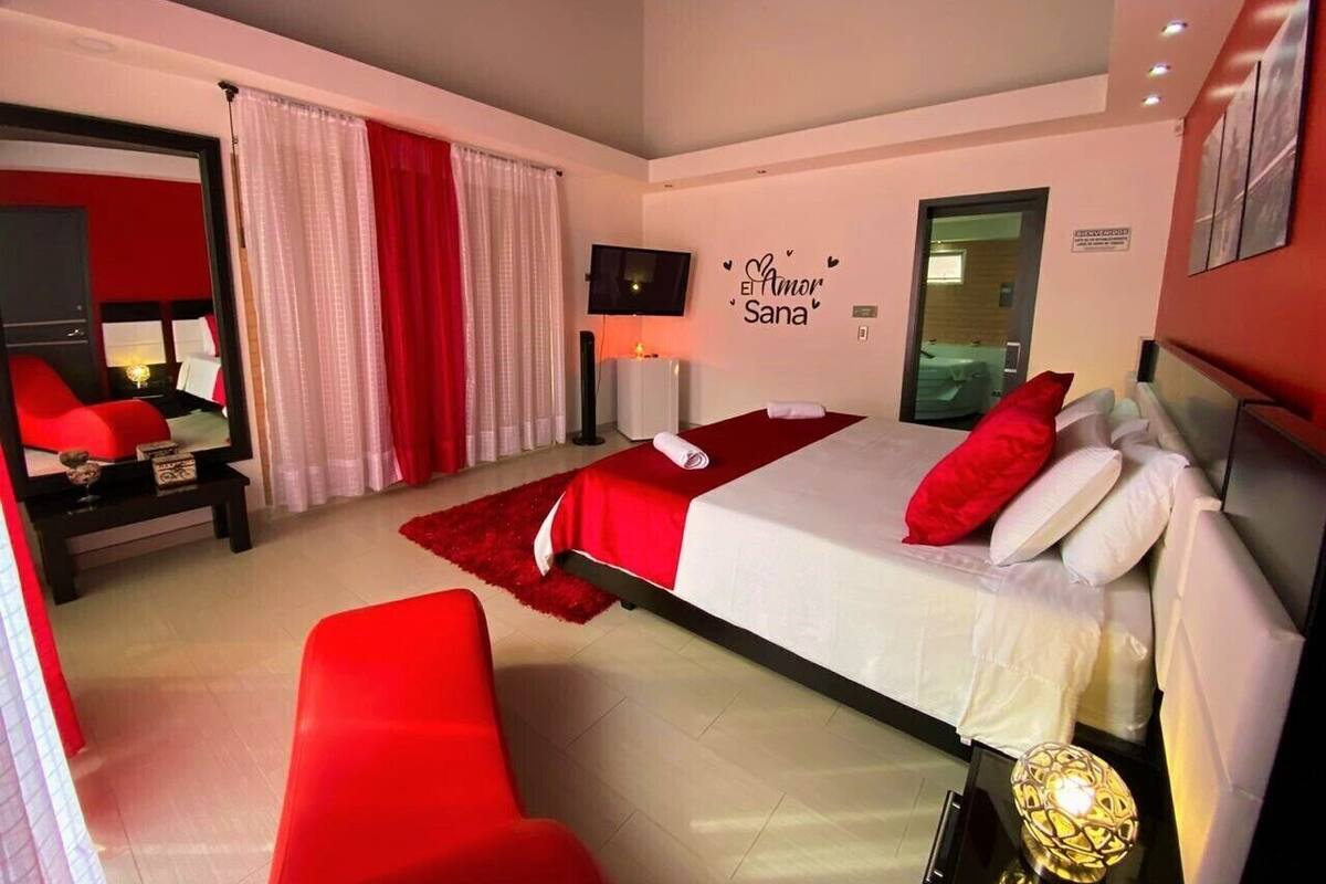 A modern hotel room with a large bed, red accents, a flat-screen TV, and a wall-mounted artwork.