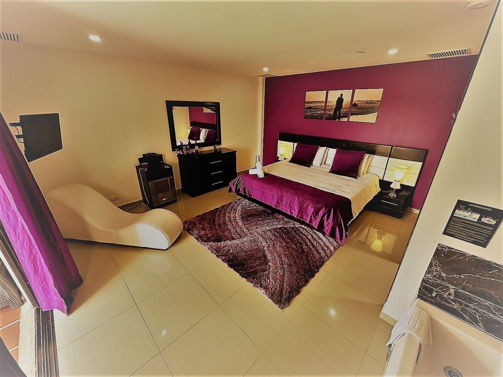 A bedroom with a bed, a chair, a dresser, a mirror, and a wall art piece.