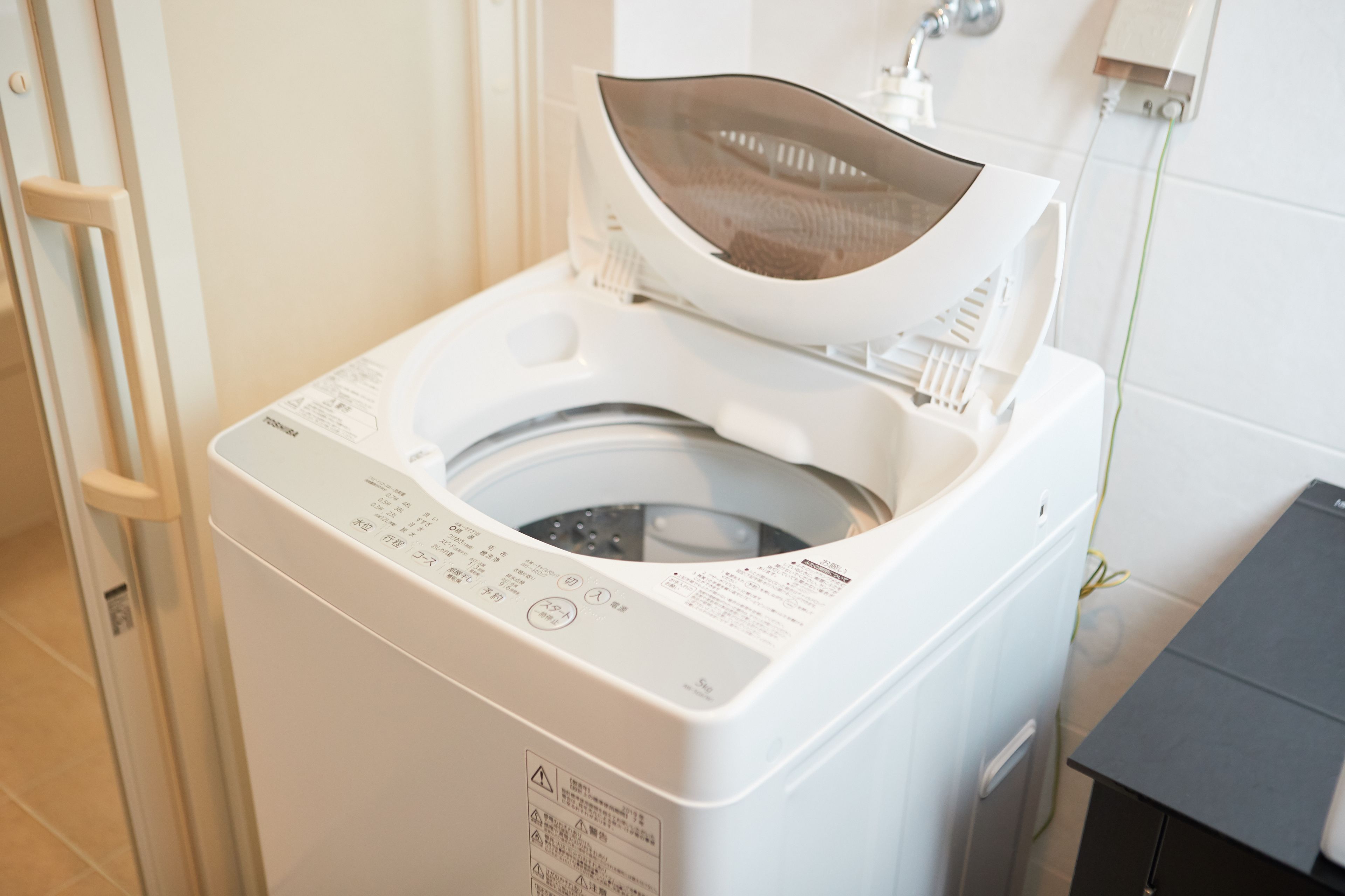 A front-loading washing machine in a bathroom with a tiled wall and a towel rack.