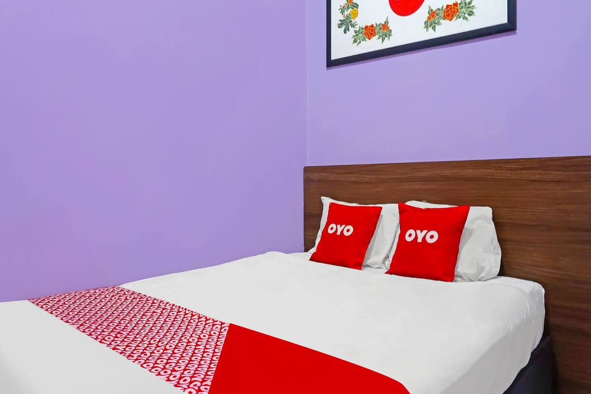 A bed with a white and red bedspread, two pillows with the word "OYO" on them, and a framed picture with the same word on the wall above the bed.