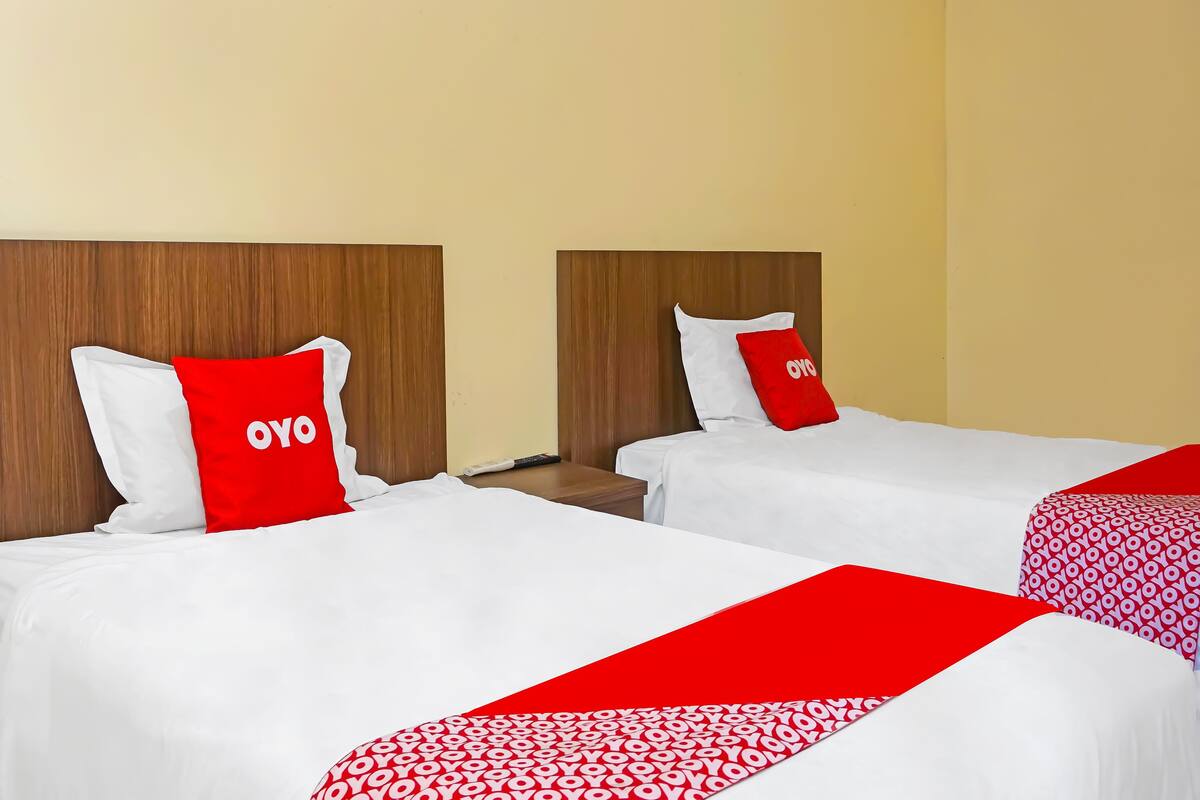 A hotel room with two beds, each with white bedding and red accents, including pillows and a red runner.
