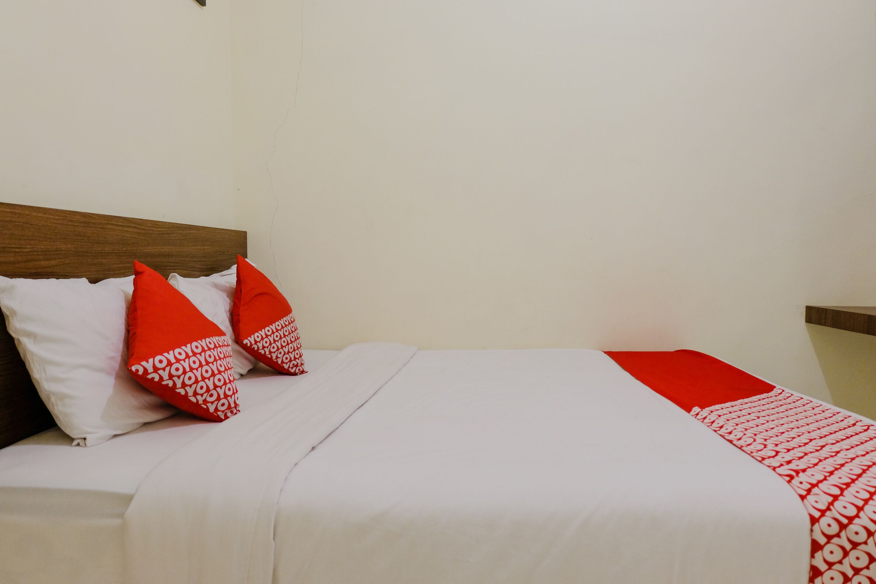 Uma cama com roupa de cama branca, almofadas vermelhas e um cobertor com padrão vermelho e branco.