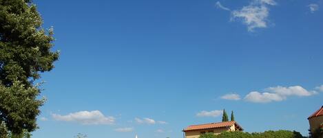 A rural landscape with a house on a hill, a clear blue sky, and a small church in the distance.