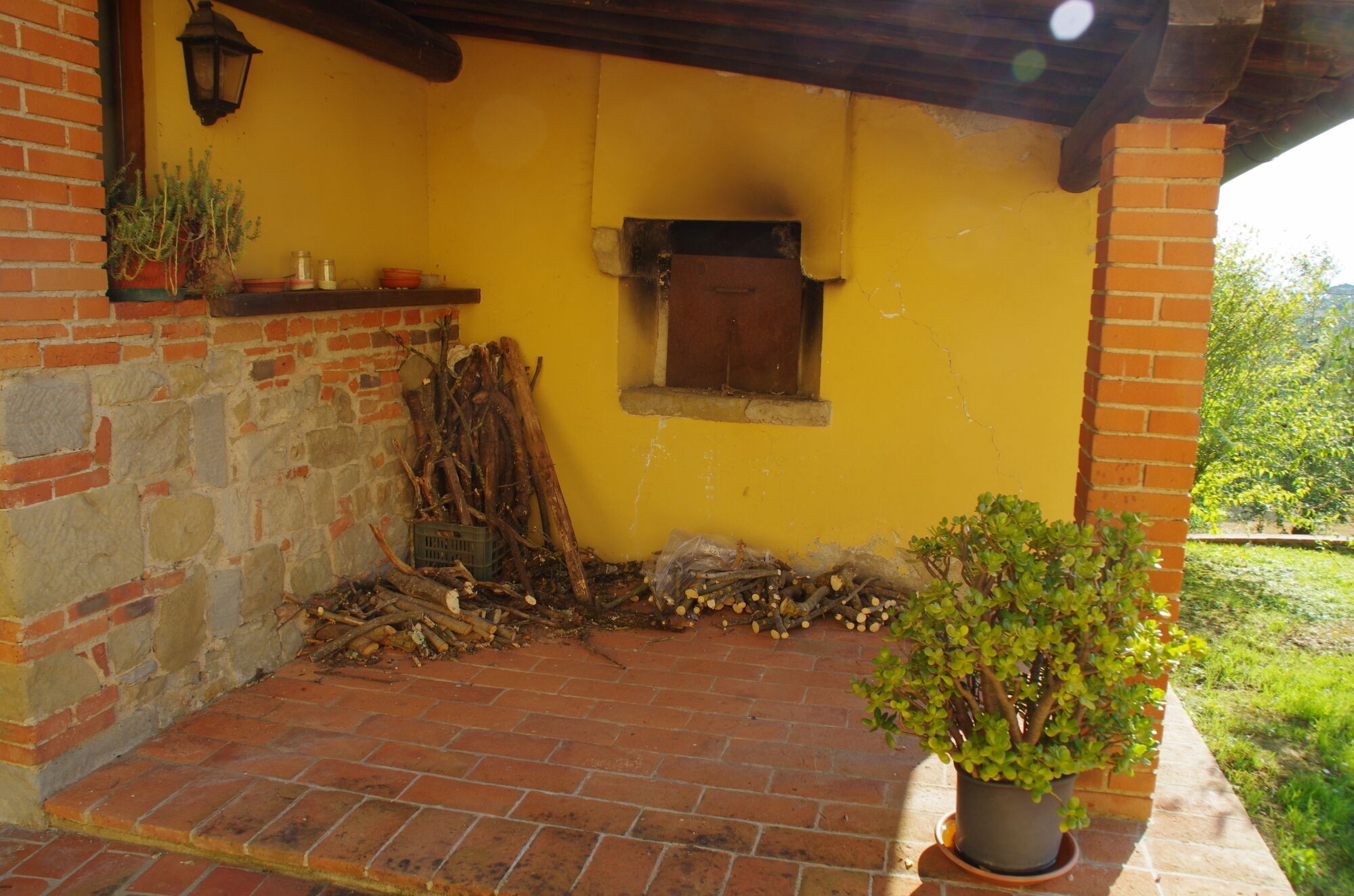 Un patio de ladrillo con una pared amarilla, una ventana pequeña y una maceta.