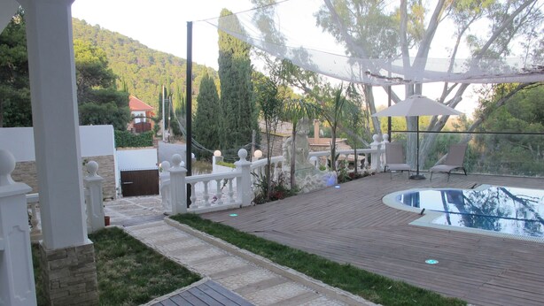 Eine Holzterrasse mit Pool, weißen Säulen und einem gepflasterten Weg.