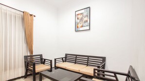 A room with a sofa, two chairs, a table, a window with curtains, and a framed picture on the wall.