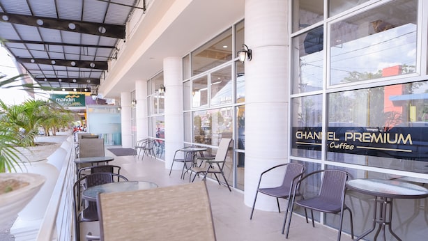 An outdoor seating area with tables and chairs, a large window with a sign for Chanel Premium Coffee, and a covered walkway with a ceiling structure. - Capital O 854 Ub Caisar Hotel (Banda Aceh)