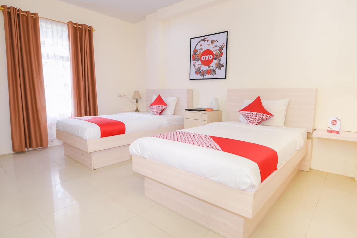 Une chambre d’hôtel avec deux lits, chacun agrémenté de draps blancs et de touches de couleur rouge, une table de chevet avec une lampe et un tableau encadré au mur.