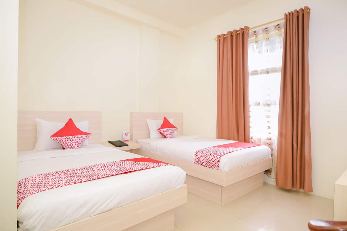 Une chambre d’hôtel avec deux lits, chacun agrémenté de draps blancs et de touches de couleur rouge, une table de chevet avec une lampe et une fenêtre avec des rideaux bruns.