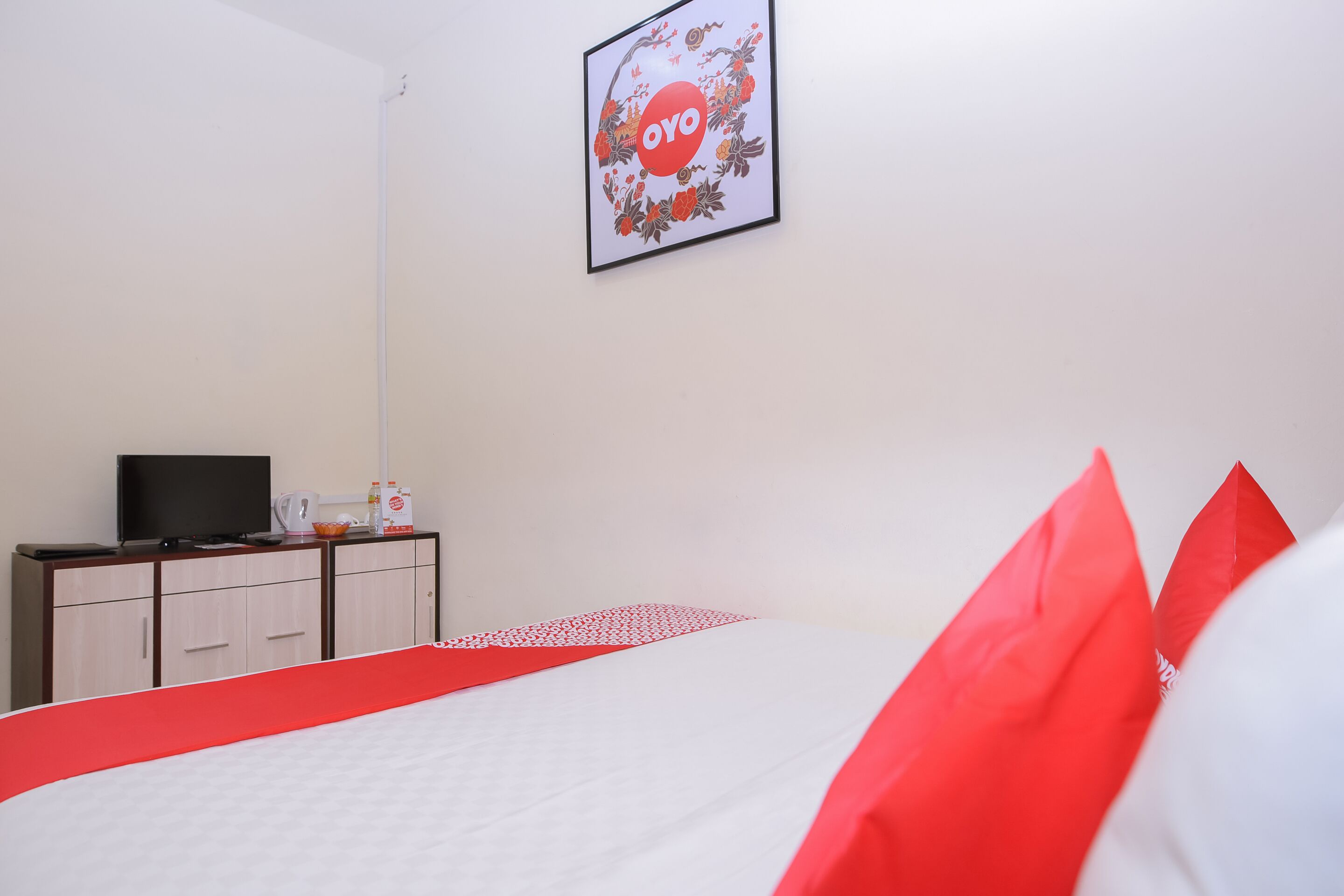 A hotel room with a bed, a TV on a wooden cabinet, and a framed picture on the wall.