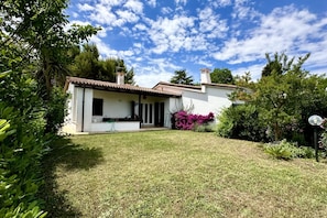 A house with a white exterior, a tiled roof, and a small garden with various plants. - N084 - Numana, villa with garden and pool (Numana)