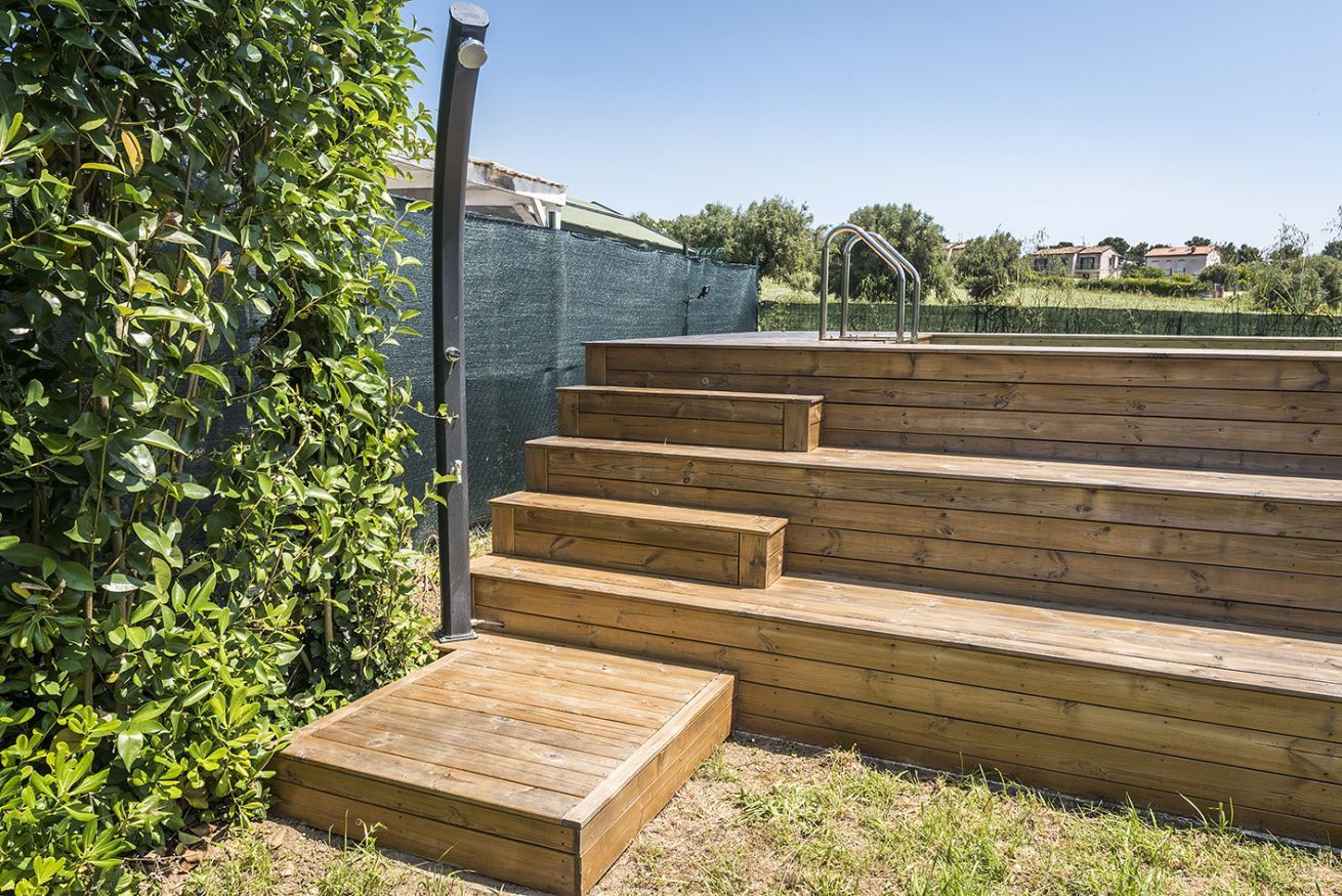 Un escalier extérieur en bois menant à une terrasse dotée d’un robinet en métal.